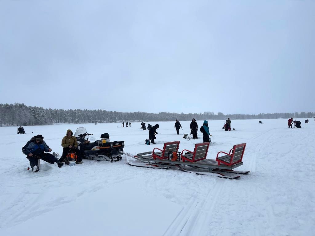 Järven jäällä pilkkijöitä. Etualalla on moottorikelkka ja sen vetämä reki.