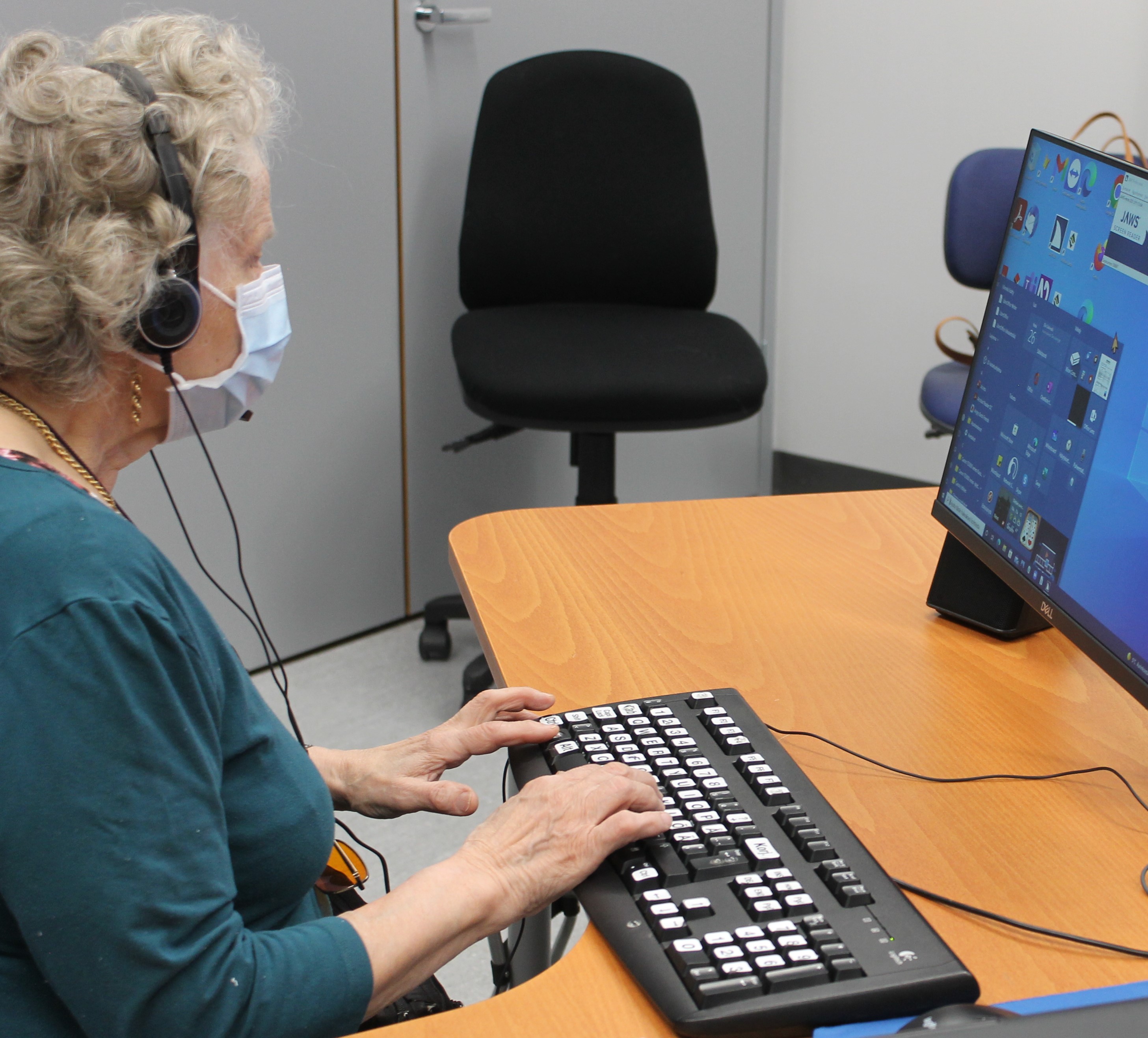 Henkilö tietokoneella kuulokkeet korvilla ja kädet näppäimistöllä